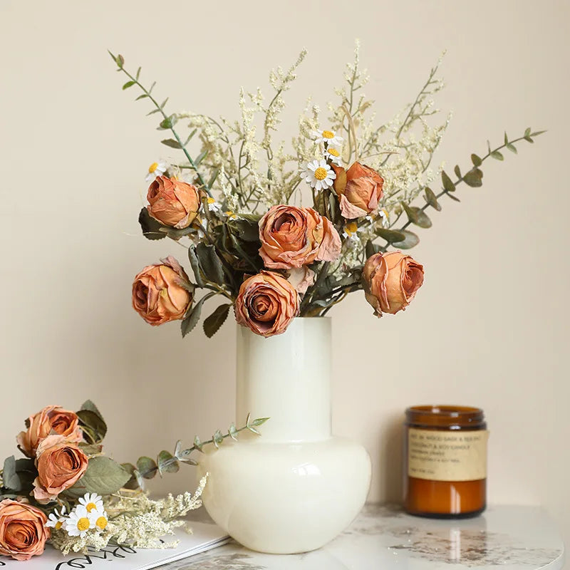 Artificial rose bouquet autumn with dried flowers in a cream vase on a decorative table
