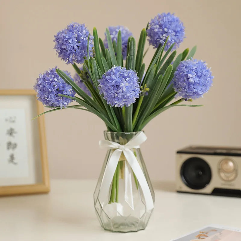 Artificial dandelion bouquet in a clear glass vase with purple flowers and green leaves
