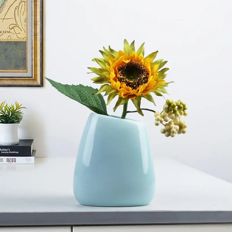 Modern light blue ceramic vase with artificial sunflower and decorative foliage