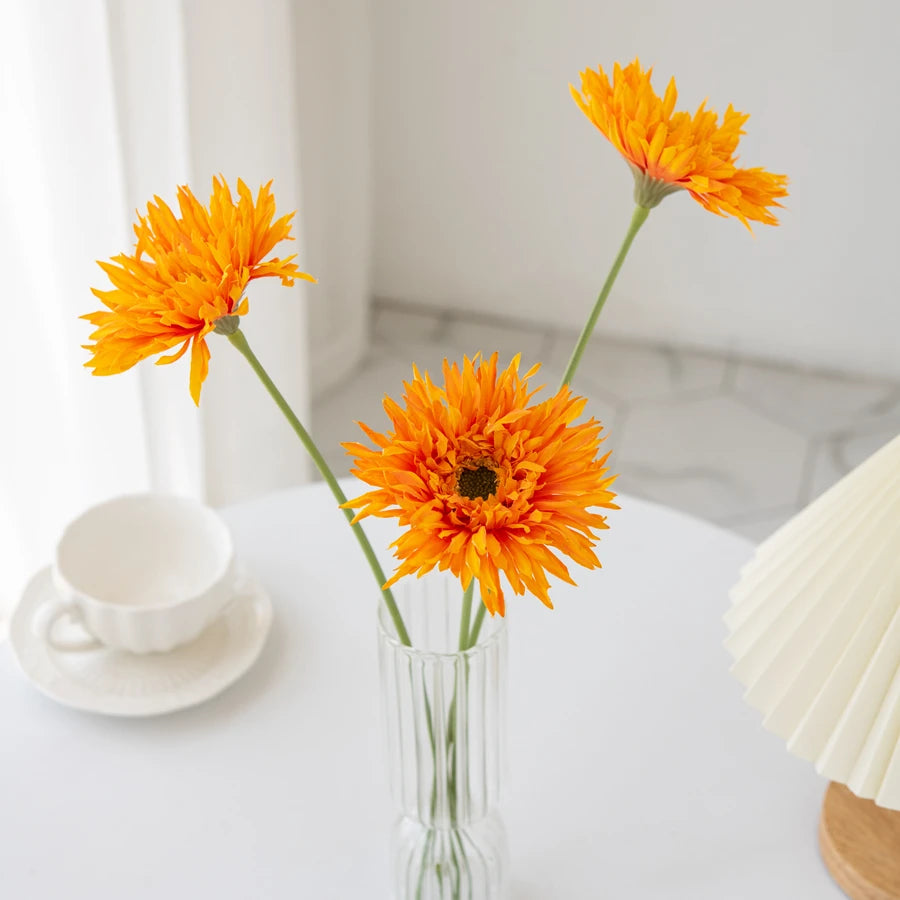 Three vibrant orange Gerbera artificial flowers 2025 arranged in a clear glass vase