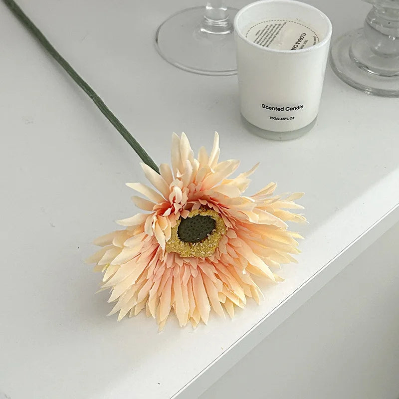Gerbera artificial flower 2025 in soft peach color with realistic petals placed beside a scented candle
