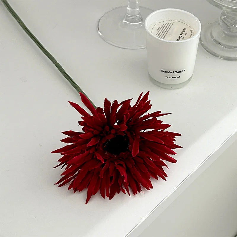 Red Gerbera artificial flower 2025 placed on a white surface beside a scented candle