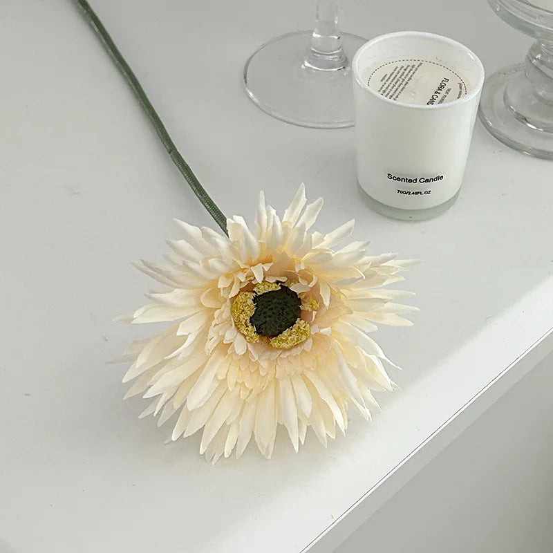 Realistic Gerbera artificial flower 2025 in cream color beside a scented candle on a white table
