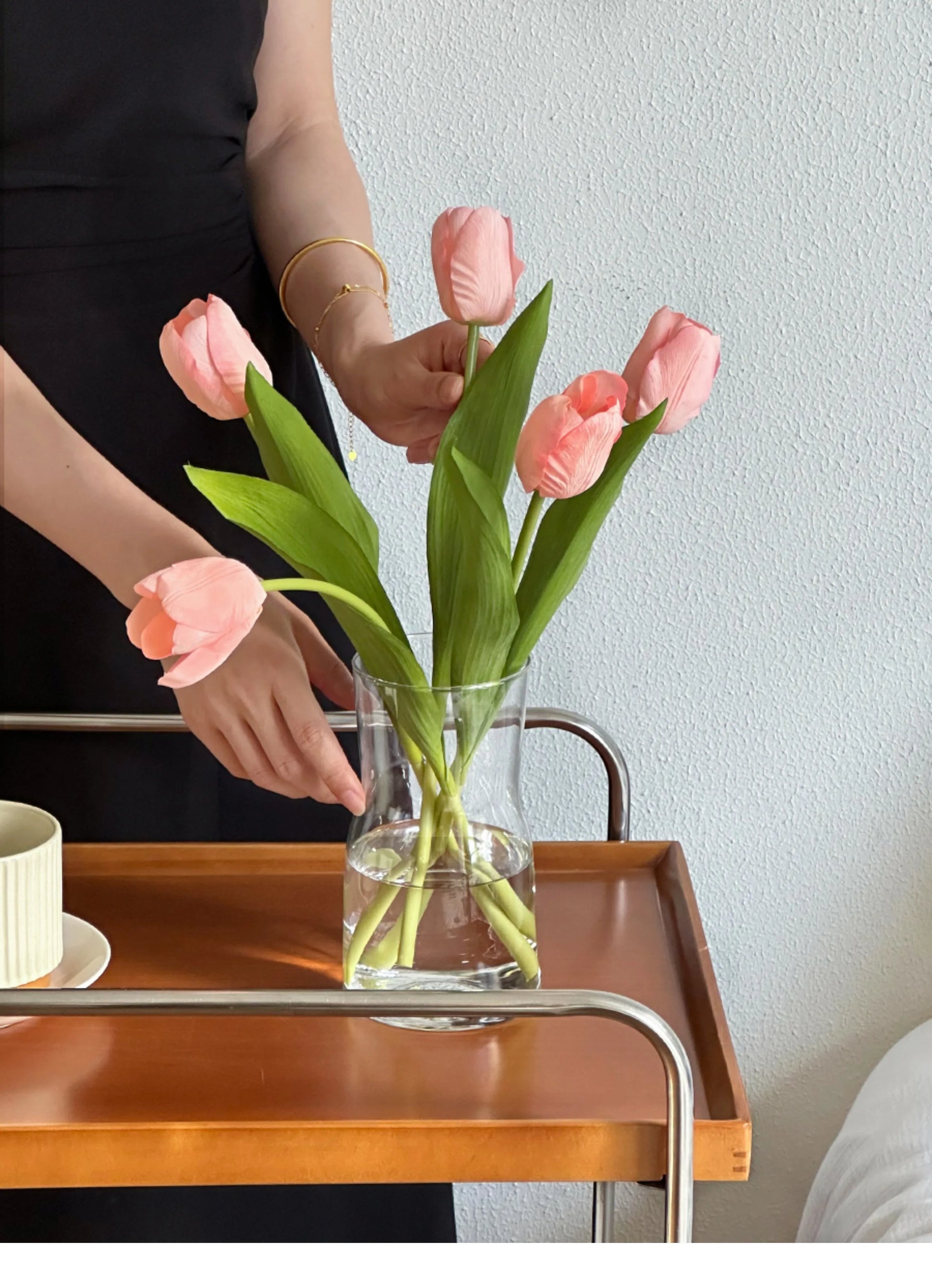 A woman arranging pink tulips in a Nordic glass vase decor on a wooden tray