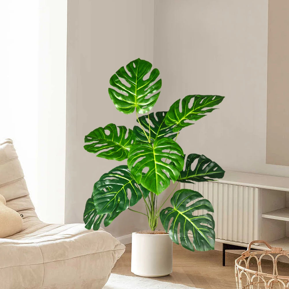 Plastic turtle leaf indoor plant in a white pot placed beside a cozy chair