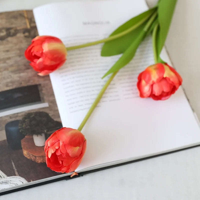 Beautiful artificial tulips in coral color placed on an open book for home decor